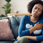 A woman sitting on a sofa, her face shows that she's having stomach issues due to levothyroxine.